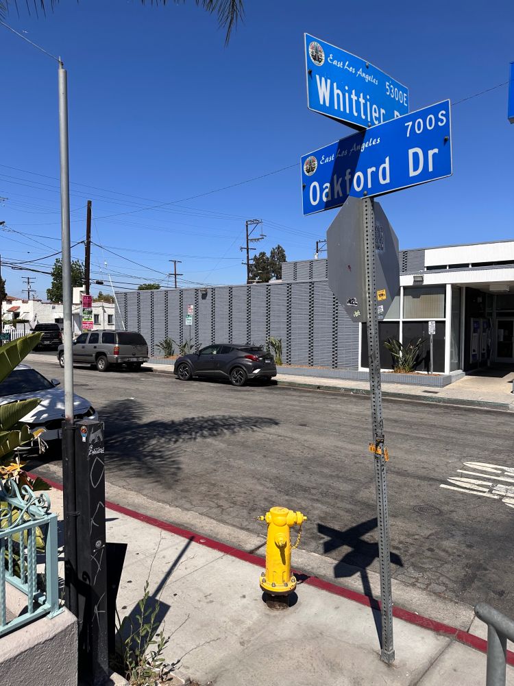 A stop sign with blue street signs above. To the left of the frame is the former stand for a payphone. The phone nor any hardware are there anymore.