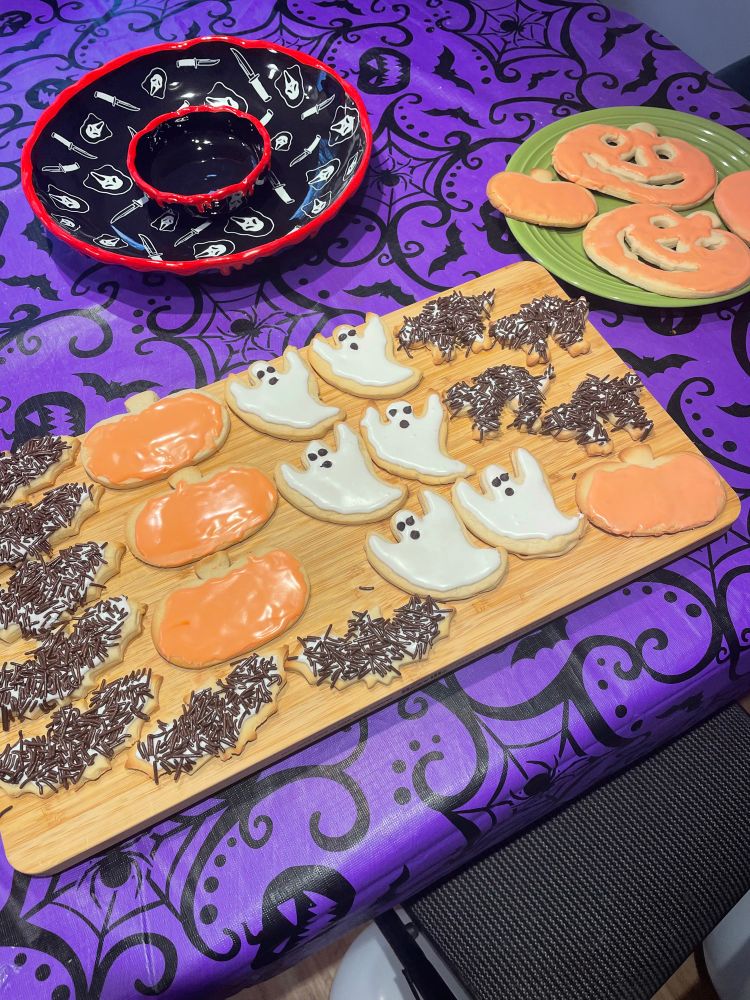 Sugar cookies on a wooden board. The cookies are shaped and decorated to look like pumpkins, ghosts, bats, and scaredy cats. 