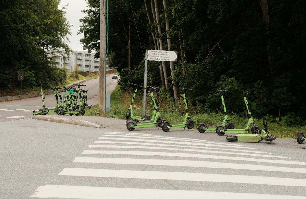 20-30 elsparkesykler parkert på tvers av fortau, fortgjengerfelt og nesten i fotgjengerfeltet.