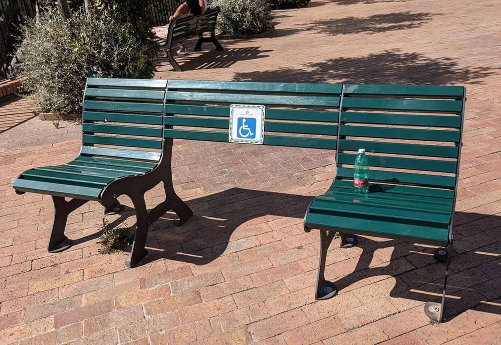 Hostile architecture park bench where the middle is removed ostensibly to create a space for wheelchairs, but obviously in actuality to make it impossible to sleep on.