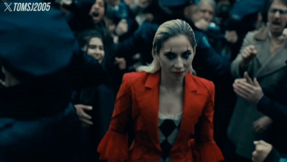 a woman in a red jacket stands in front of a crowd with tomsj 2005 written on the bottom right