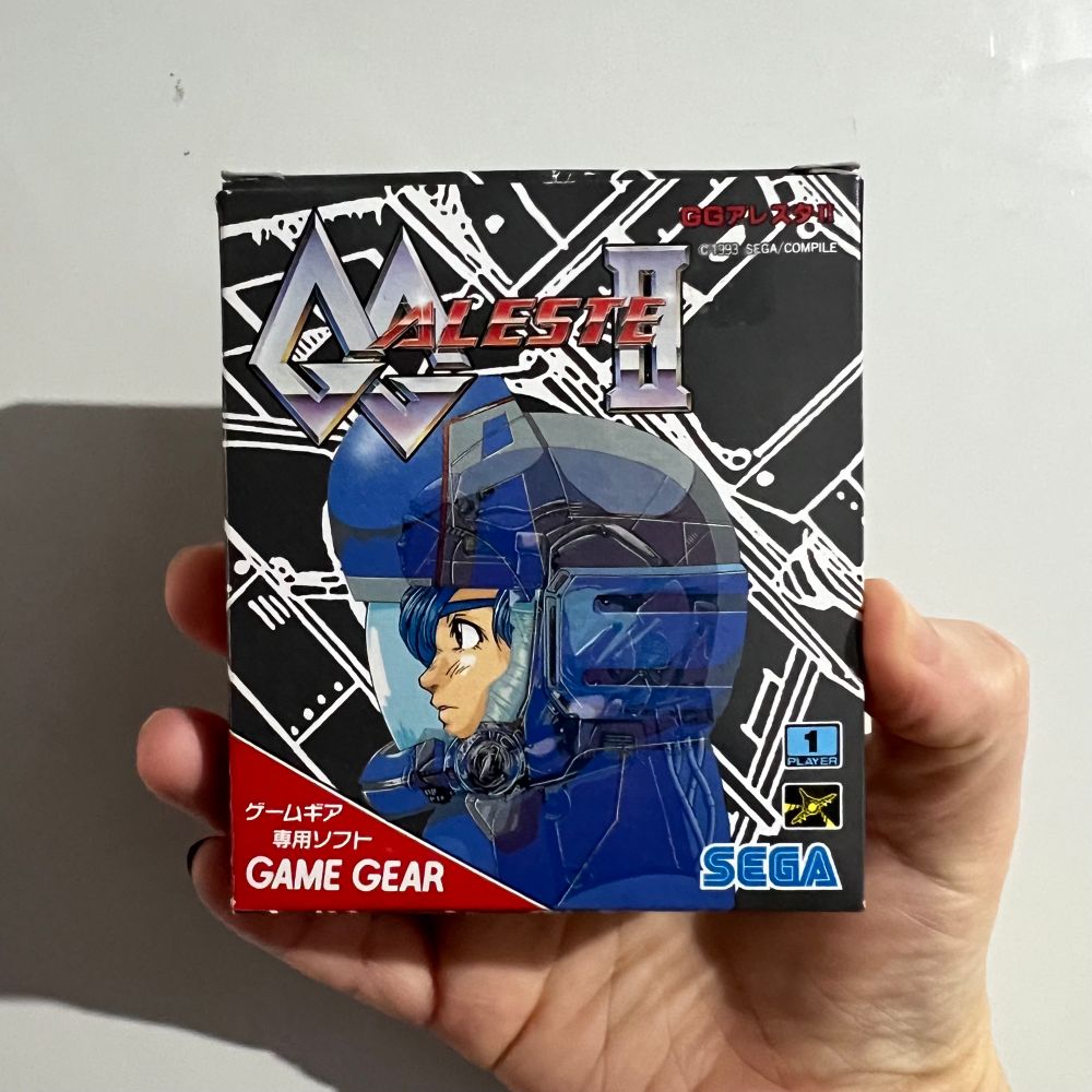 Holding up a copy of “GG Aleste 2” (or Power Strike II in EU) for the Game Gear.

The cover illustration features a side-on view of its protagonist, wearing a blue space suit, superimposed over a background which looks like a wireframe representation of their craft.