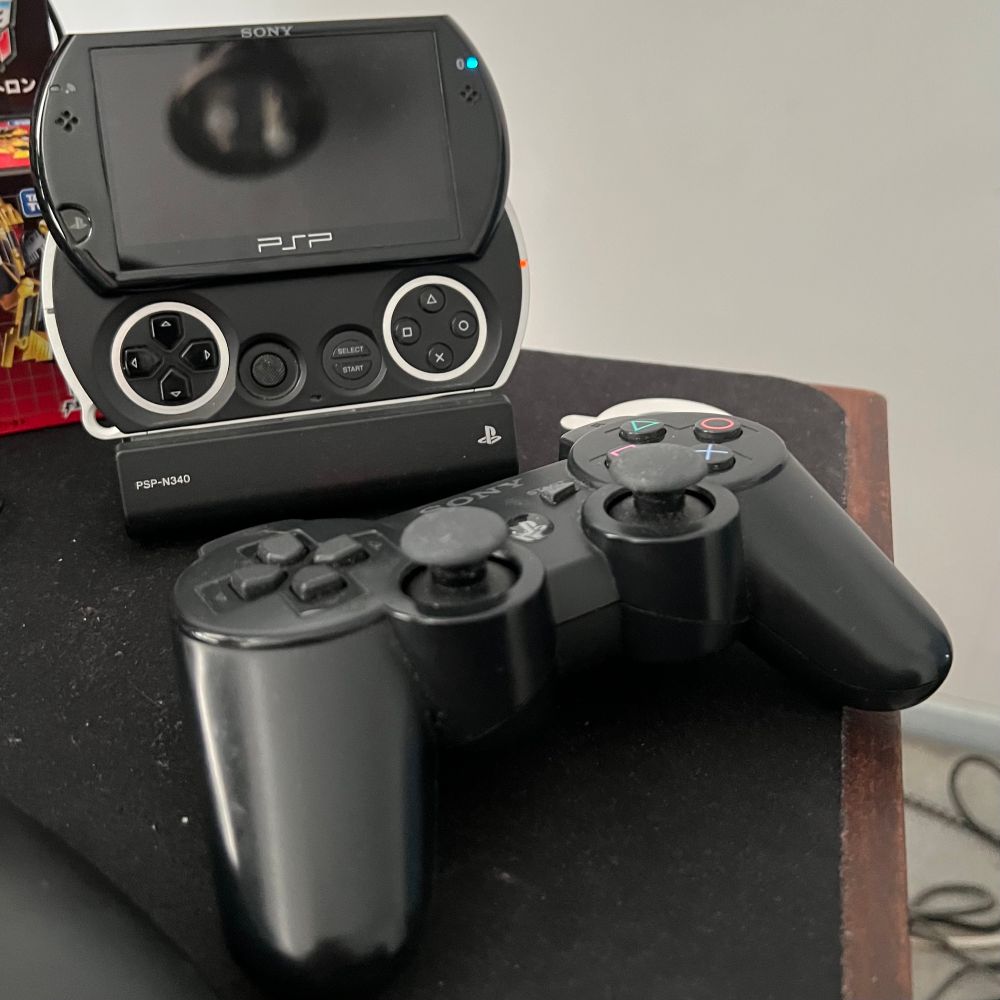 Photo of a PSP Go inside its dock with a Dual Shock 3 pad sitting in front of it.