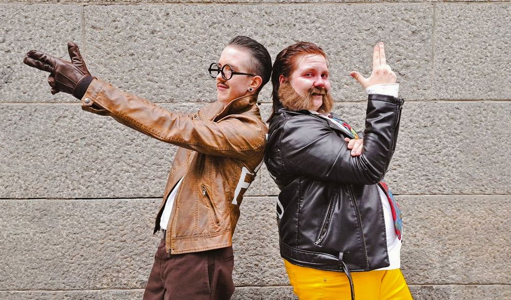 Photo of a Kim Kitsuragi and a Harry Du Bois cosplayer taken in Tracon 2025. Kim has his hands straight pointed out like a gun, and Harry is pointing fingerguns towards the sky.