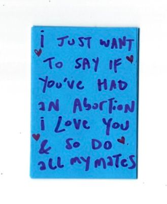a blue piece of (folder) paper that reads (in purple) "I just want to say if you've had an abortion i love you & so do all my mates". There are four hearts scribbled near the corners. 