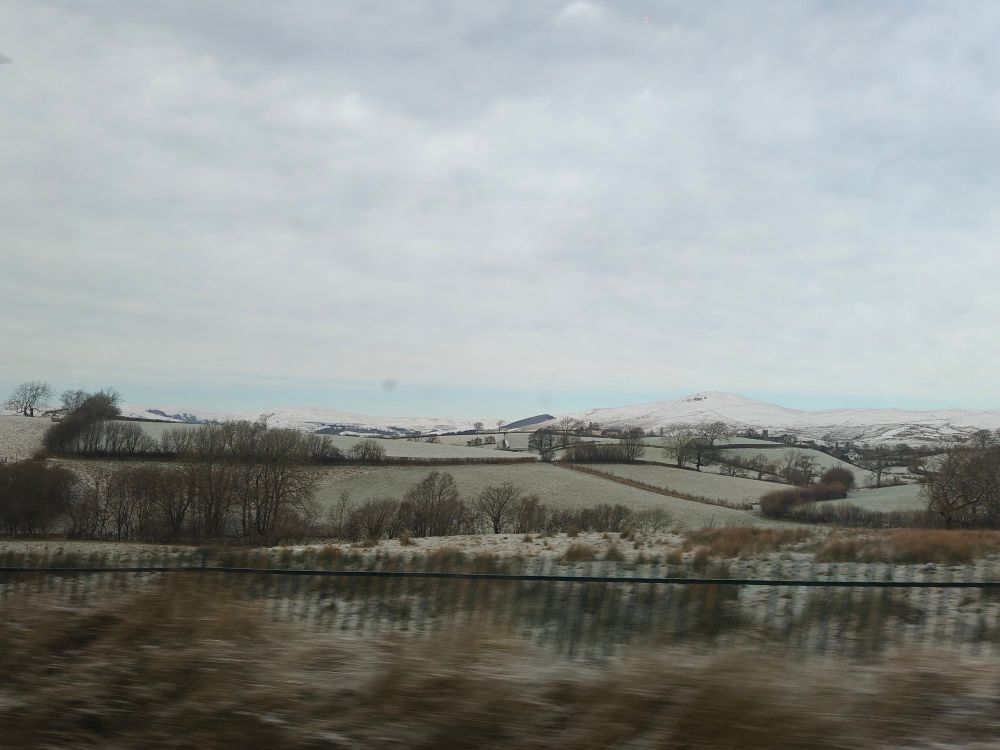 Photo of fields with snowy hills in the distance 