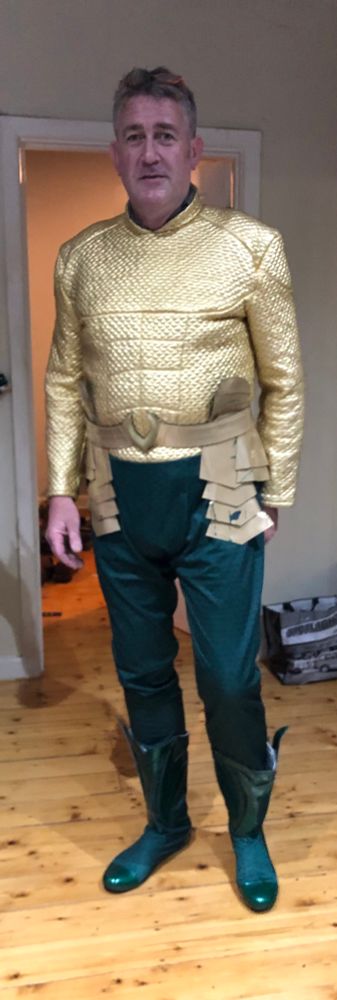 My dashing husband is dressed in an Aquaman costume. The pants are dark green velvet and the top is a padded golden synthetic material. He has fake body armour with side panels, a vinyl belt and shiny green boots. 