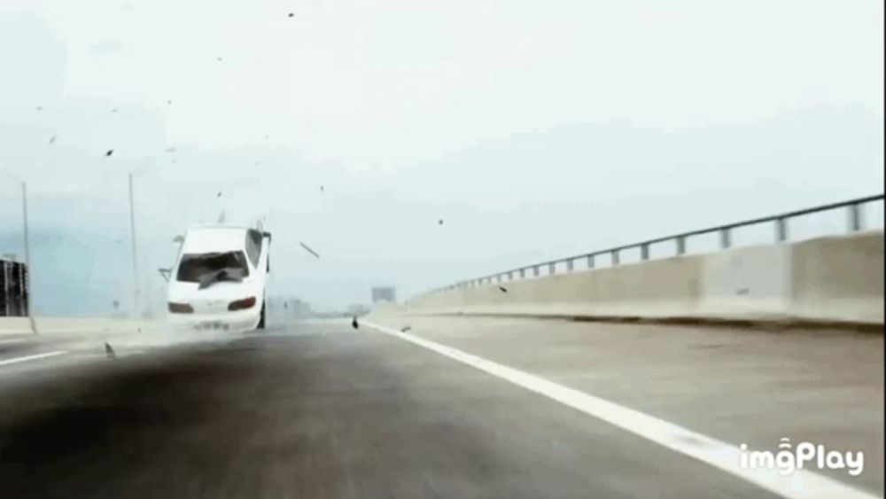 a white car is driving down a highway and crashing into something .