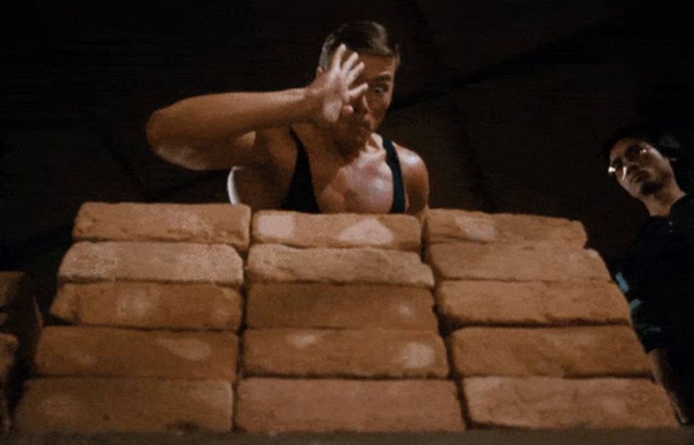 a man standing in front of a pile of bricks with his hand up