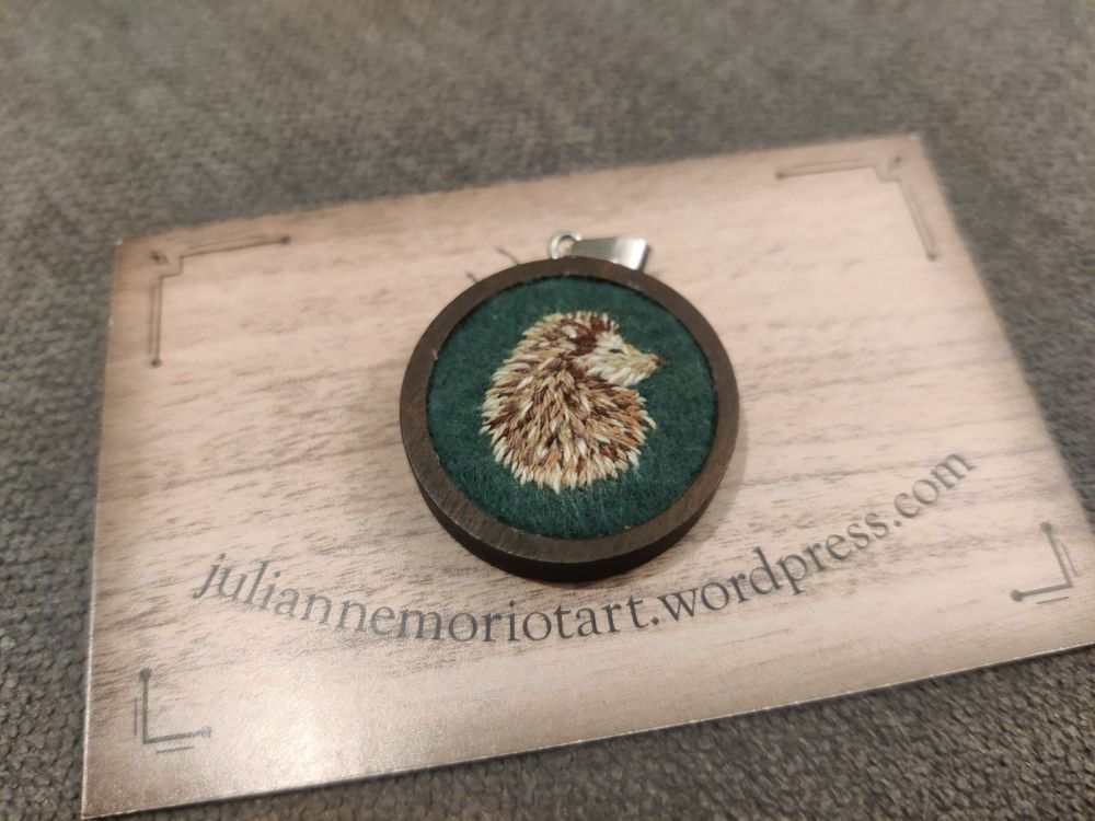 Médaillon brodé représentant un hérisson posé sur la carte de visite de @petitdeux.bsky.social