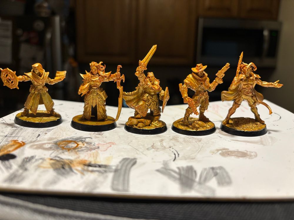Five miniatures painted gold. The top halves of the miniatures shine just a little bit brighter than the bottom halves.