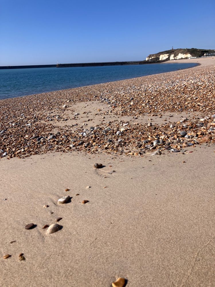 Low tide sand and pebbles, curved line of the sea, distant cliffs  