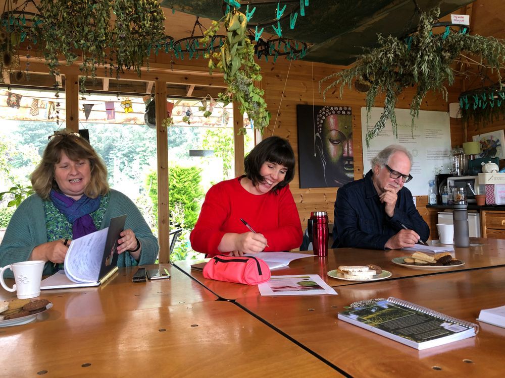 Smiling people writing at one of my workshops at Dilston Physic Garden, in Herbology House with herbs hanging from the ceiling