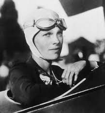 Amelia Earhart sitting in plane cockpit, wearing aviator's goggles