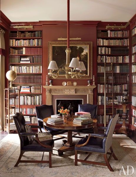 Mississippi private home library with floor to ceiling bookshops full of books, a fireplace, a round table with armchairs around it, and books stacked on table and chair