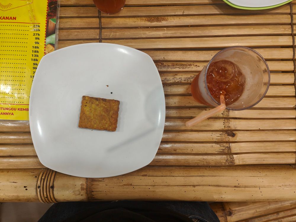 A plate containing a single tempe and a glass of iced tea.
