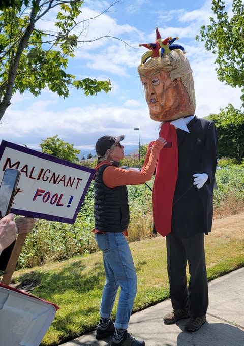 Sign reads 'Malignant fool' while protestor straightens Donold costume tie.