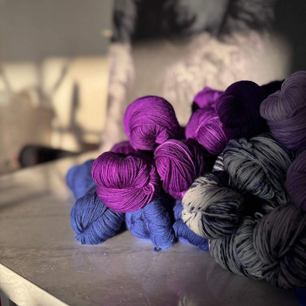 Jewel toned skeins of blue and purple yarn glow in the setting sunlight. 