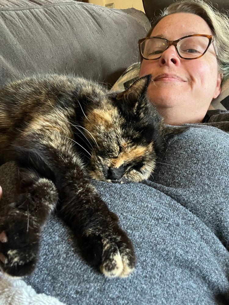A small tortie cat asleep stretched out over a woman’s chest 