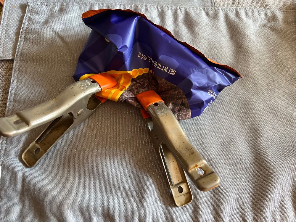 A bag of tortilla chips, held closed with two woodworking clamps.