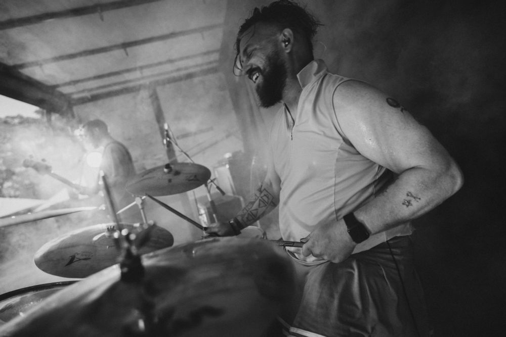 Ein weißer Mann mittleren Alters mit wilden Haaren und Bart in einem Tennis-Dress hinter einem Schlagzeug. 