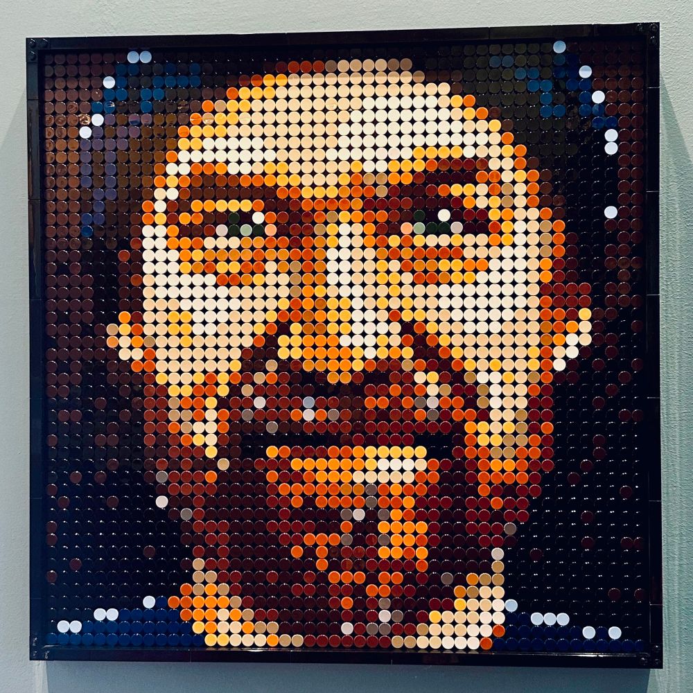 A portrait of a man done completely in Lego pieces. We are close to the face, and he is looking at the viewer with a clear gaze, sparkle in his eye, and smirk on his lips.
