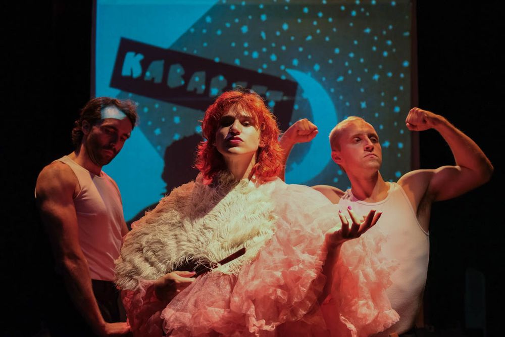 Candy (Flo Wiedenbach), a cabaret performer, wears large pink frills and holds a white feather fan