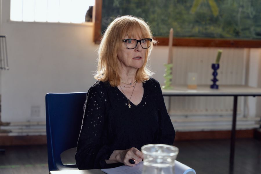 Maud (Wendy Nottingham) sits at a table looking stricken. 