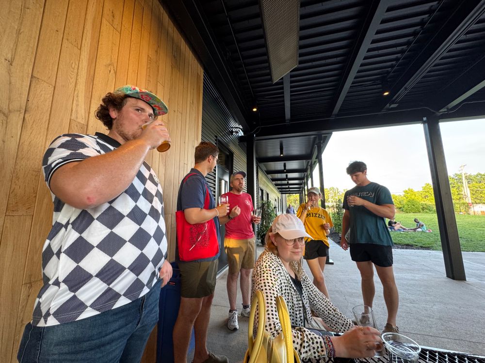 An angle of folks standing near the table, all with drinks in their hands. 