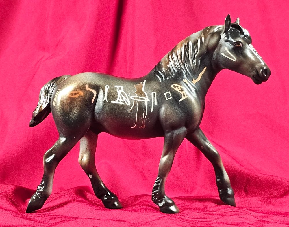 A photo of a Pebbles scale Stone model horse on the drafter mold. He has hieroglyphics painted on his side. His body color is a bronze-tinged dusty black with dapples.