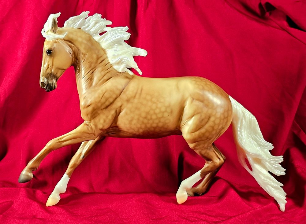 A photo of a Breyer horse on the Criollo mold. He is called Future is Bright, and is a dappled palomino with two socks. Special run from Breyerfest 2025.