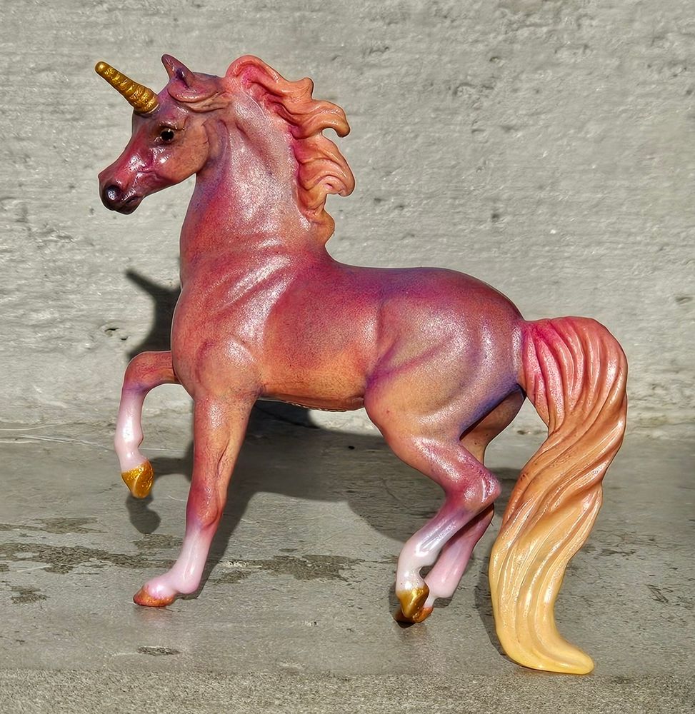 A photo of a Breyer Stablemates model horse. It is the G2 prancing Morgan with a unicorn horn. He is being customized with pastels and is currently in shades of yellow, orange, pink, and purple.