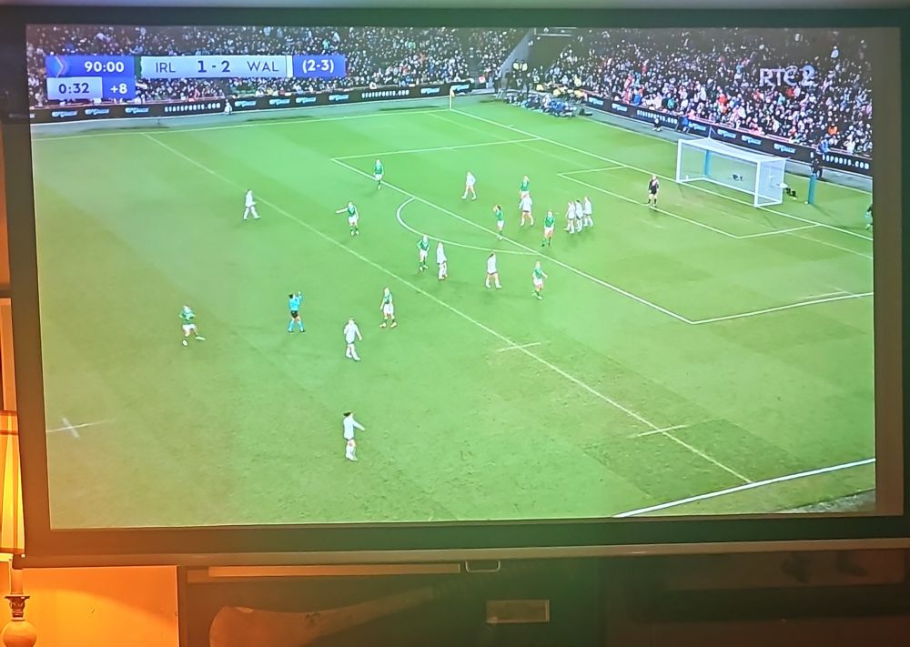 Large screen with Ireland vs Wales match being played. 
The clock shows 90 minutes played with 8 minutes additional time. 
Score: IRL 1-2 WAL (2-3)
