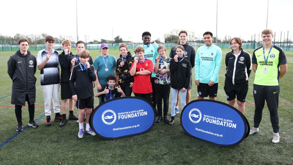 A group picture of all of the targeted kicks participants with their medals, along with Diego Gomez, Carlos Baleba and their coaches. Many of them are biting their medals!