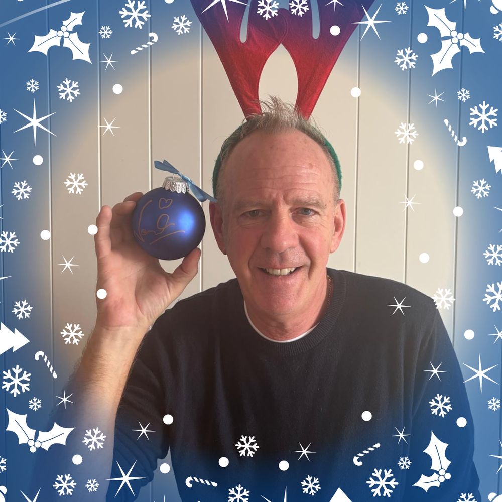 Norman Cook, wearing a festive pair of reindeer ears, holds up his signed Christmas bauble