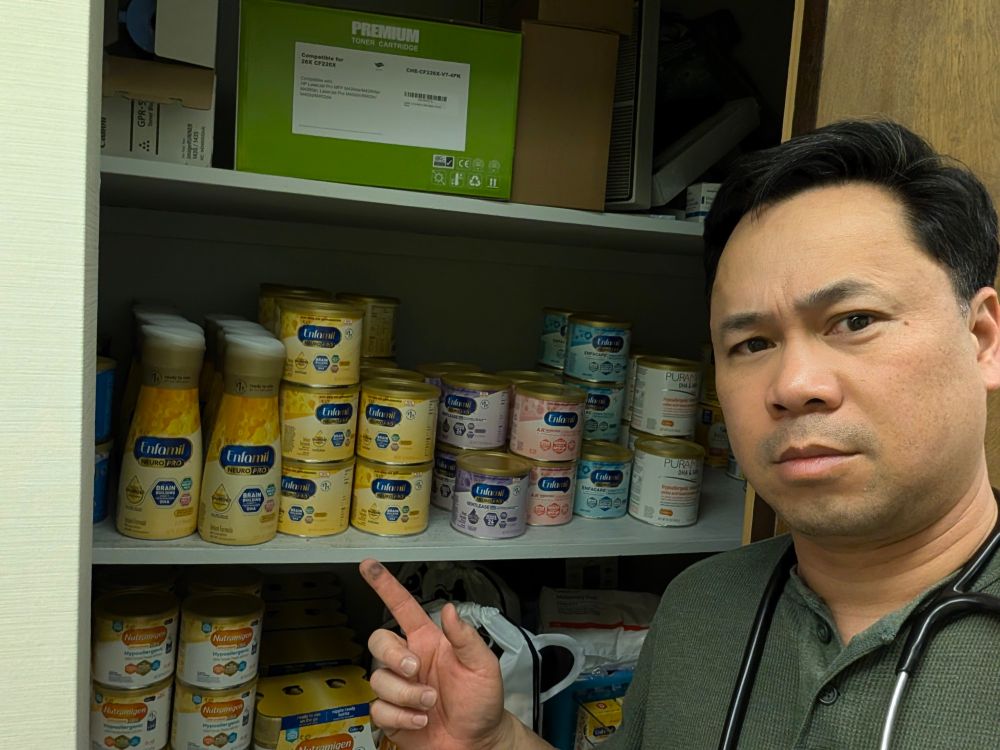 An image of me pointing to a closet full of Enfamil cans of various types and colors. 
