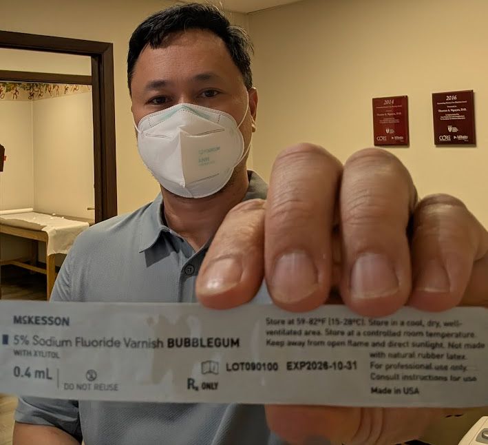 Image of me. A handsome Asian male with a white KN95 mask hosling up a small white package of bubblegum flavored sodium fluoride varnish.