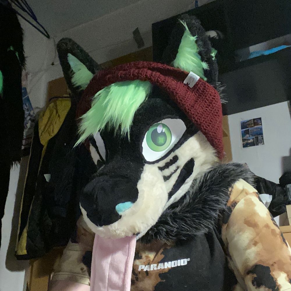 Gaege. Fursuit head. Green hair, long tongue, green eyes, wearing a beanie 