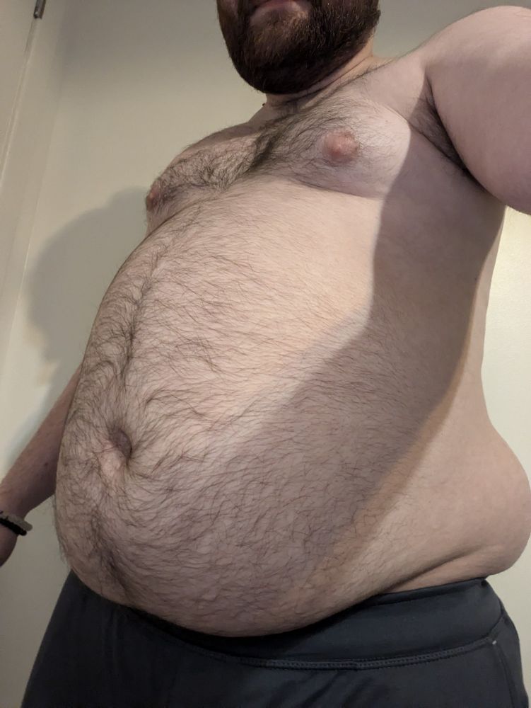 Selfie at a lower angle looking upwards of a chubby male, shirtless. 