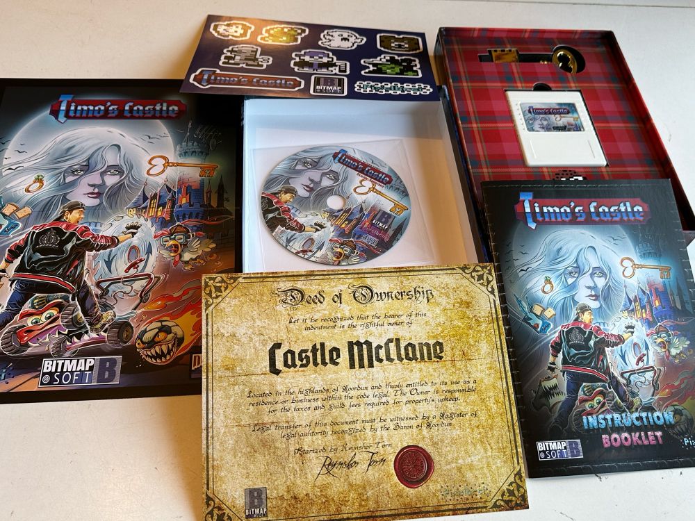 Contents of Timo’s Castle game for Commodore 64 - castle deeds, manual, art print, stickers, soundtrack CD, USB drive in the shape of a golden key, white game cartridge, game manual