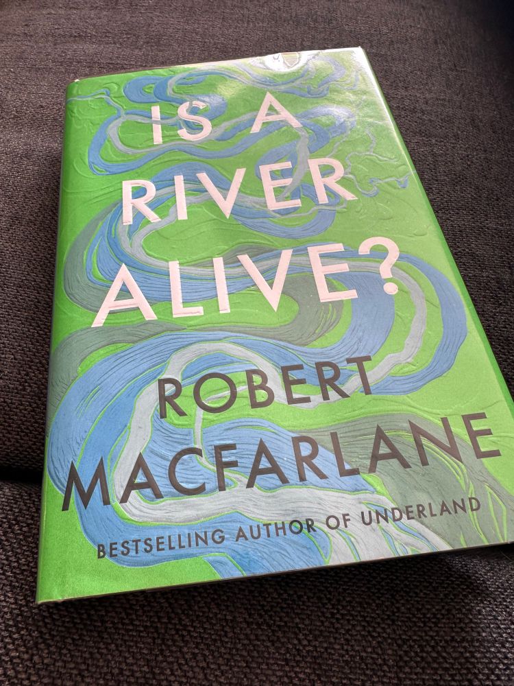 Cover of the book Is a River Alive by Robert Macfarlane. The cover is green and blue with swirls and eddies of rivers intertwined beneath the title. The design is reminiscent of the Frick maps of the Mississippi that trace the multiple paths of the river over time. 