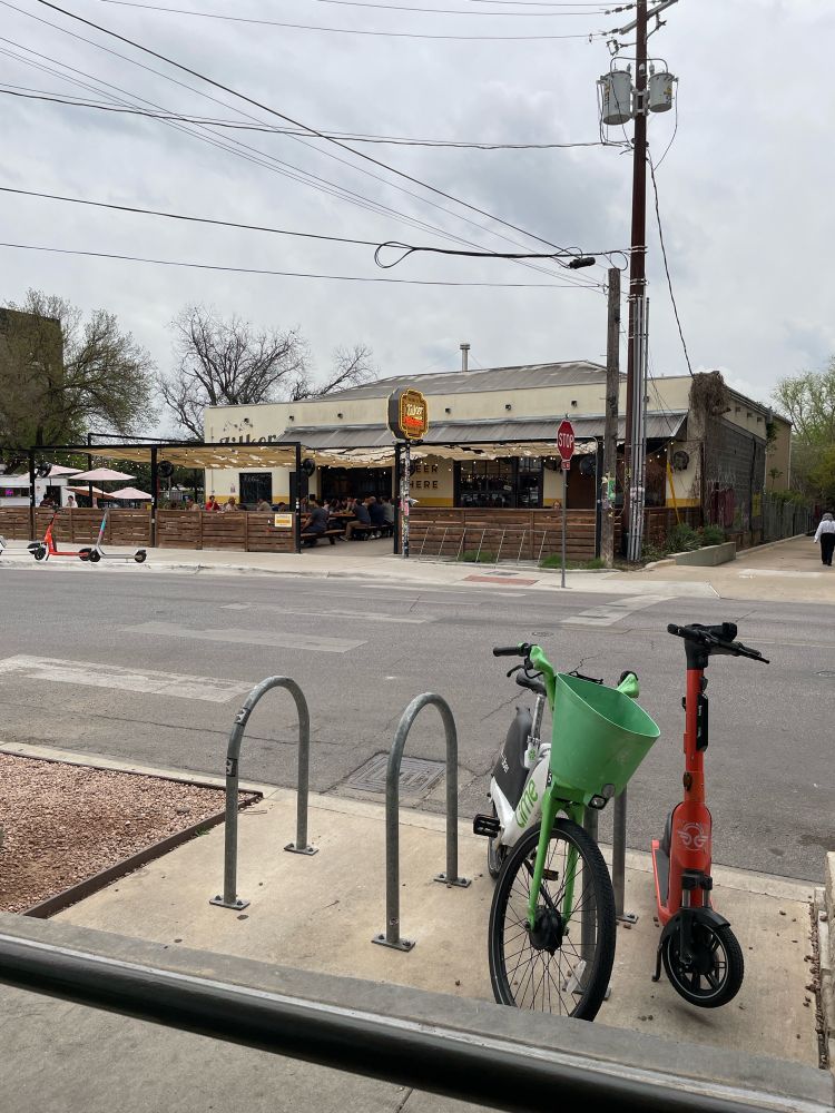 A street side photo of a bar with a bike, a scooter, and cloudy windy skies.