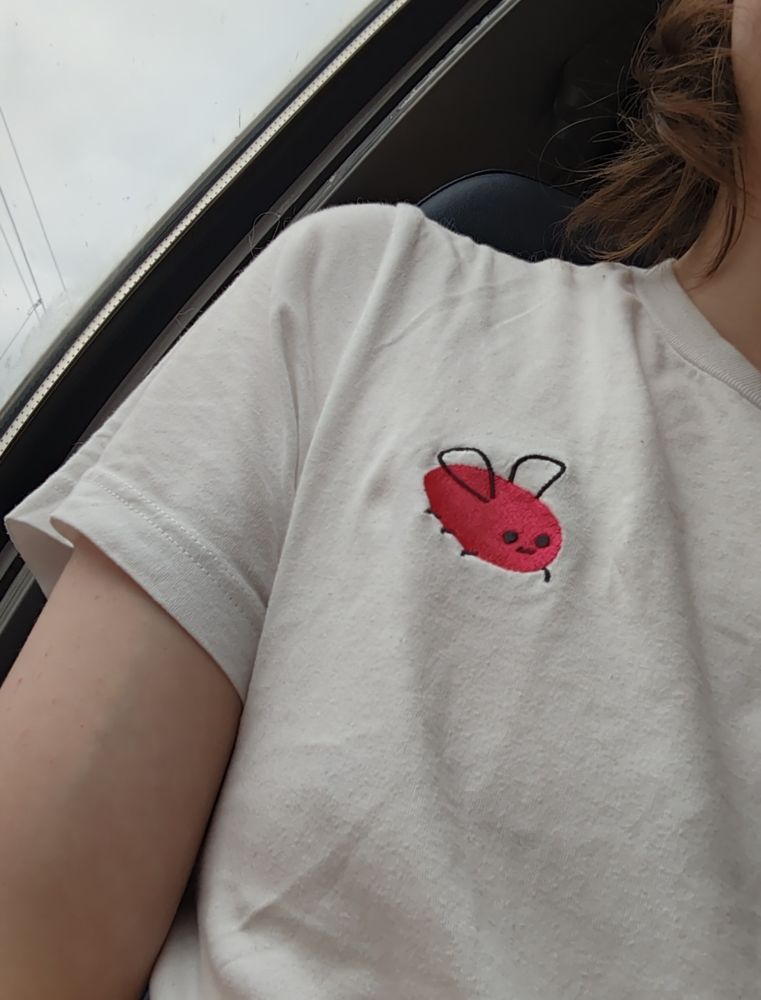 Picture of my shoulder, white t-shirt with embroided red egg shaped bug