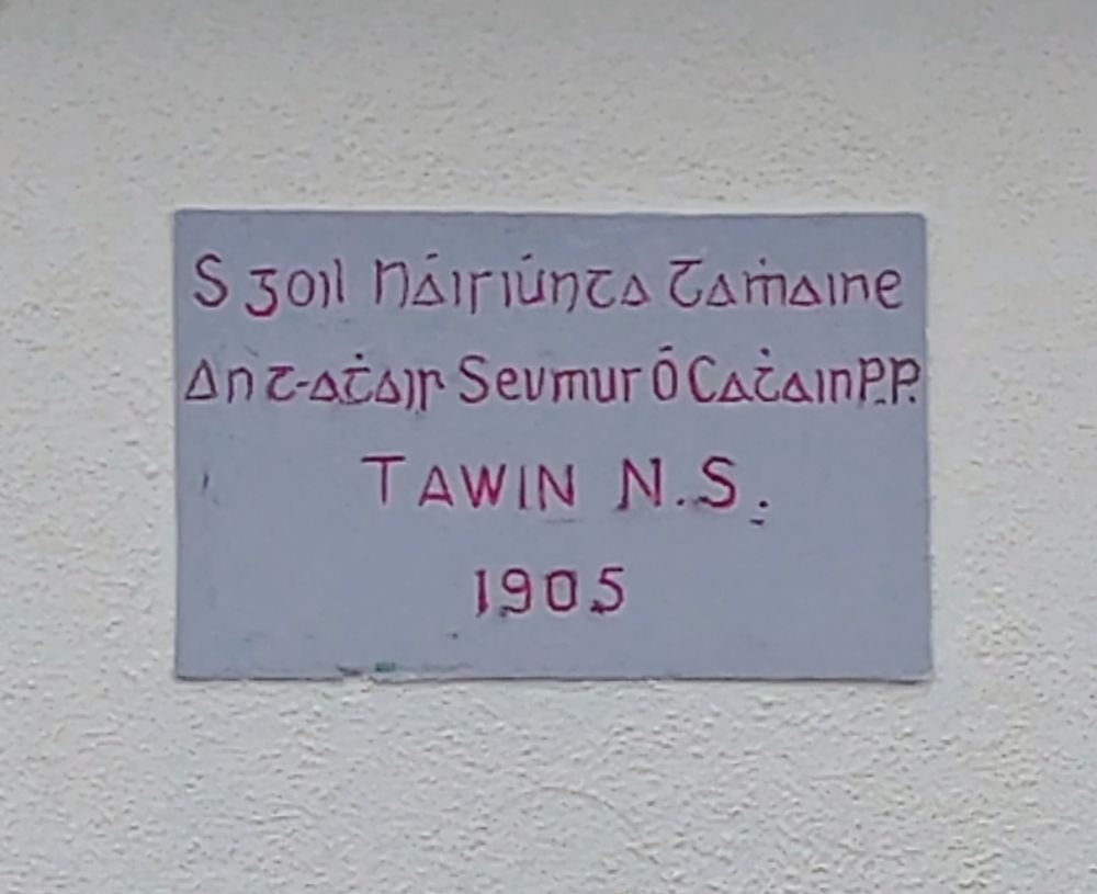 A plaque reading Sgoil Náisiúnta Tamhaine / An t-athair Seumus Ó Cathain PP /  Tawin NS / 1905 in the cló Gaelach.