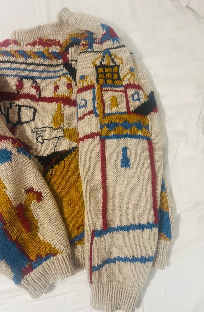Beige jumper on a white background, the focus is a sleeve with an image of a tower and halleys comet overhead in blue, gold and red