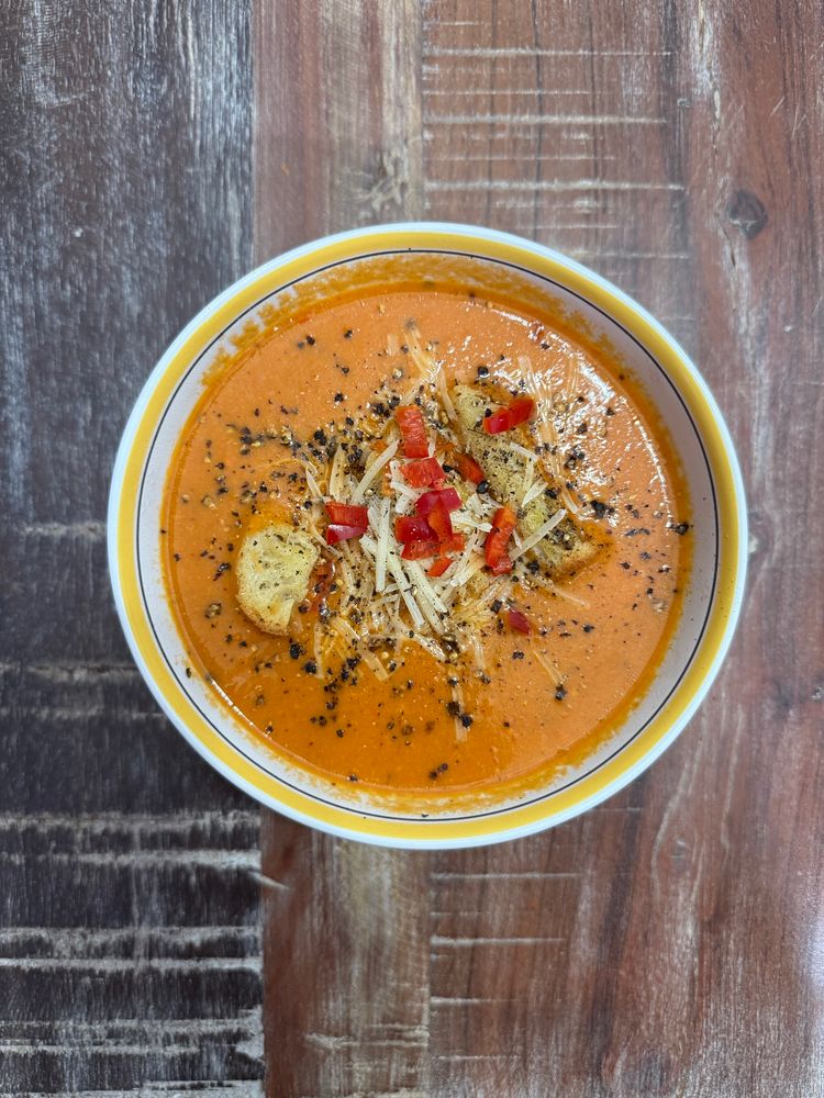 spicy roasted red pepper soup in a bowl with diced red jalapeños, homemade croutons, black pepper, and shredded cheese 