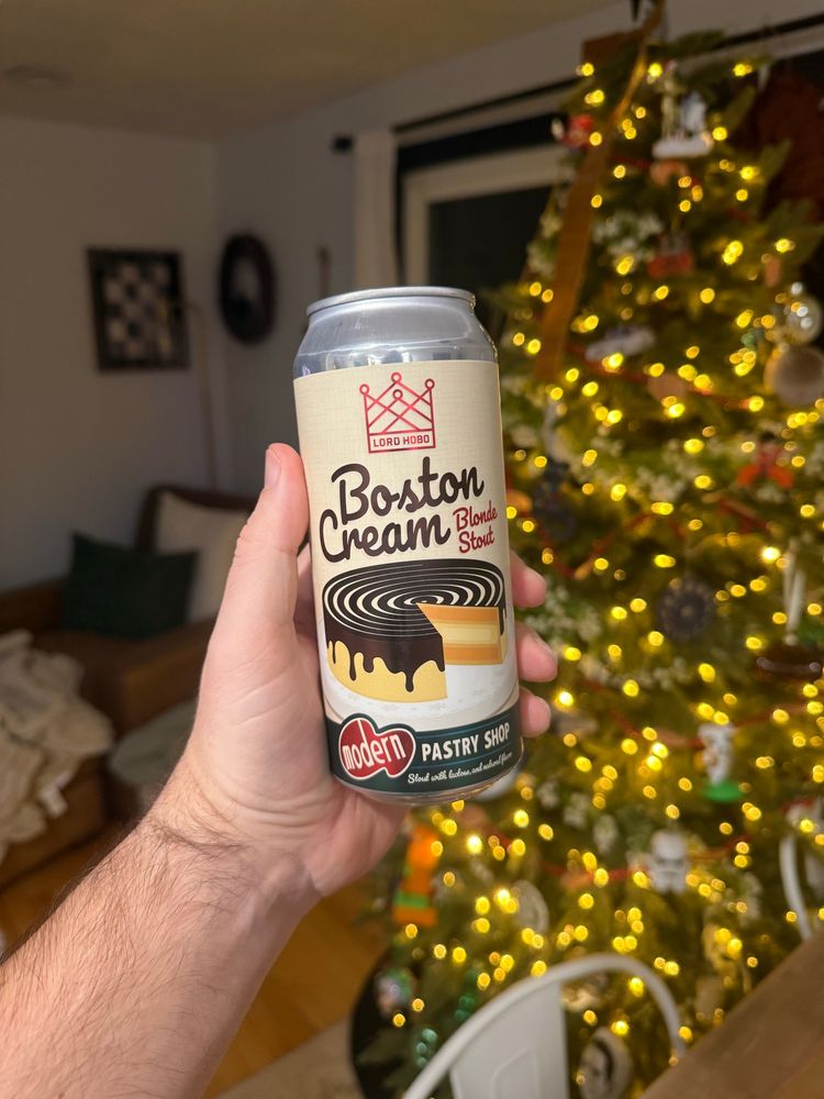 Holding a can of lord hobo Boston cream blonde stout with a lit Christmas tree in the background 