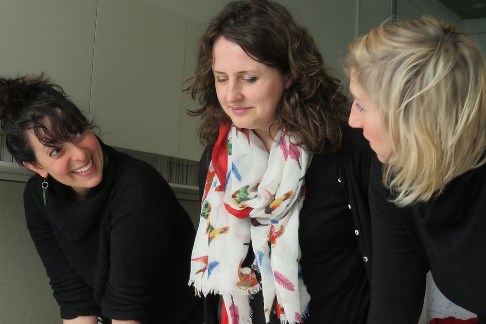 Three people are looking at something that is out of shot. They are laughing and smiling with each other.
