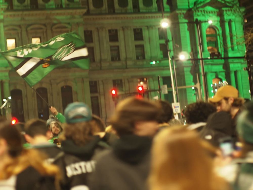A man waves an eagles flag in front of city hall, Philadelphia amidst a large crowd