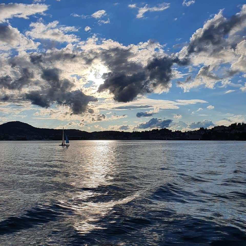 Lake Luzerne, Switzerland,  taken from a boat a couple of hours before sunset with connecting scattered clouds. There is a blue and white sailboat ⛵️ in the distance.  